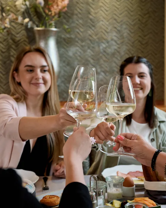 Gruppo di amici brinda con vino bianco a tavola in un ristorante con cibo